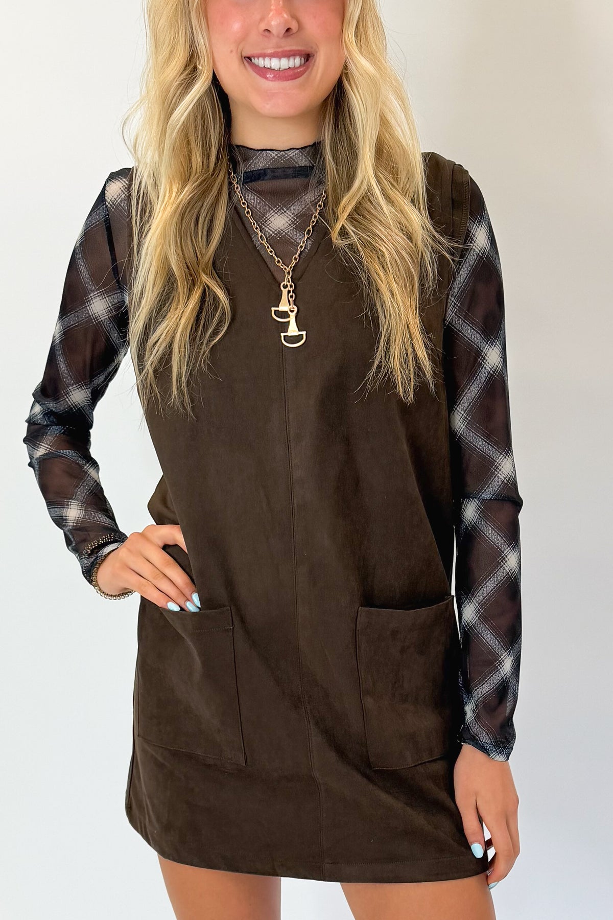 Front detail view of woman wearing Swagger Boutique’s Brown Suede V-Neck Mini Dress with Navy Plaid Mesh Top against white studio background.
