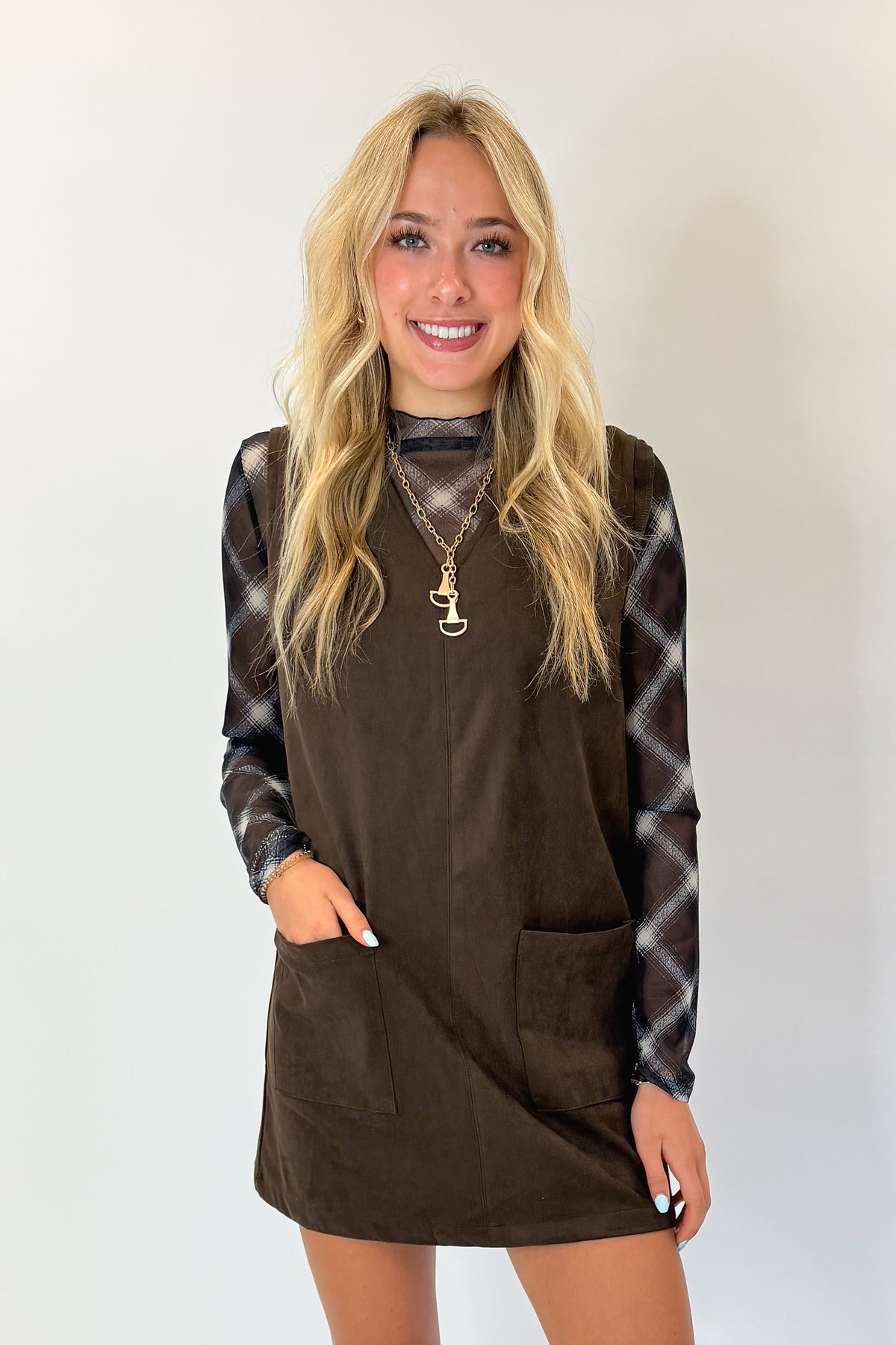 Front view of woman wearing Swagger Boutique’s Brown Suede V-Neck Mini Dress with Navy Plaid Mesh Top against white studio background.