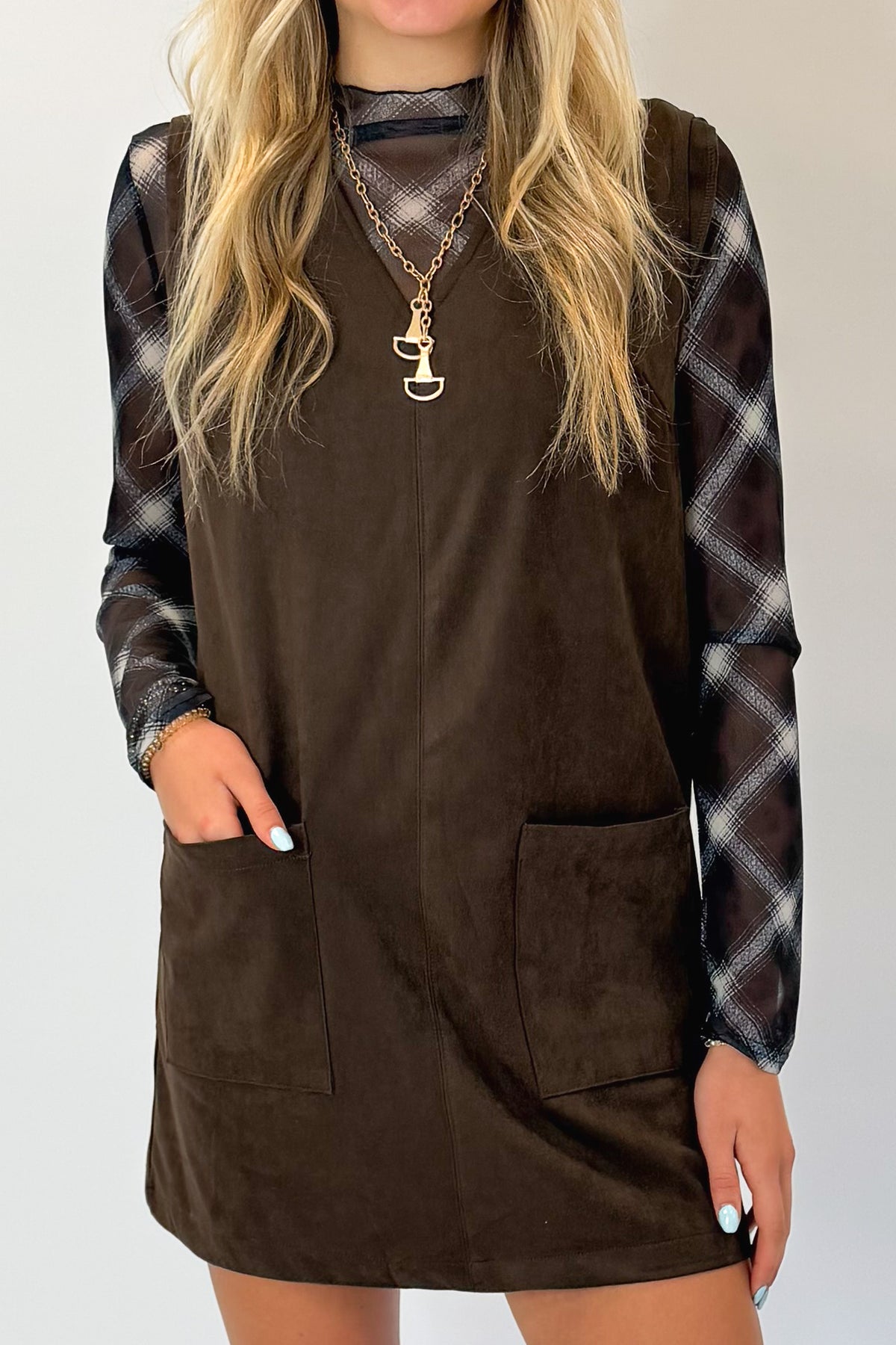 Front detail view of woman wearing Swagger Boutique’s Brown Suede V-Neck Mini Dress with Navy Plaid Mesh Top against white studio background.