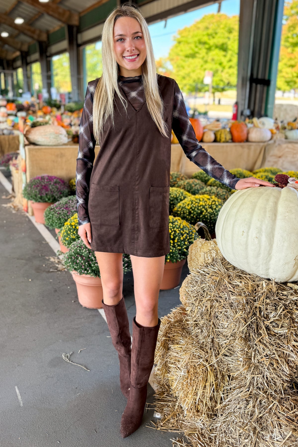 Front view of woman wearing Swagger Boutique’s Brown Suede V-Neck Mini Dress with Navy Plaid Mesh Top standing at a pumpkin patch.