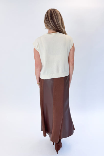 Back view of woman wearing Swagger Boutique’s Cream Sleeveless Button Up Sweater with Brown Suede &amp; Leather Midi Skirt by THML against white studio background.