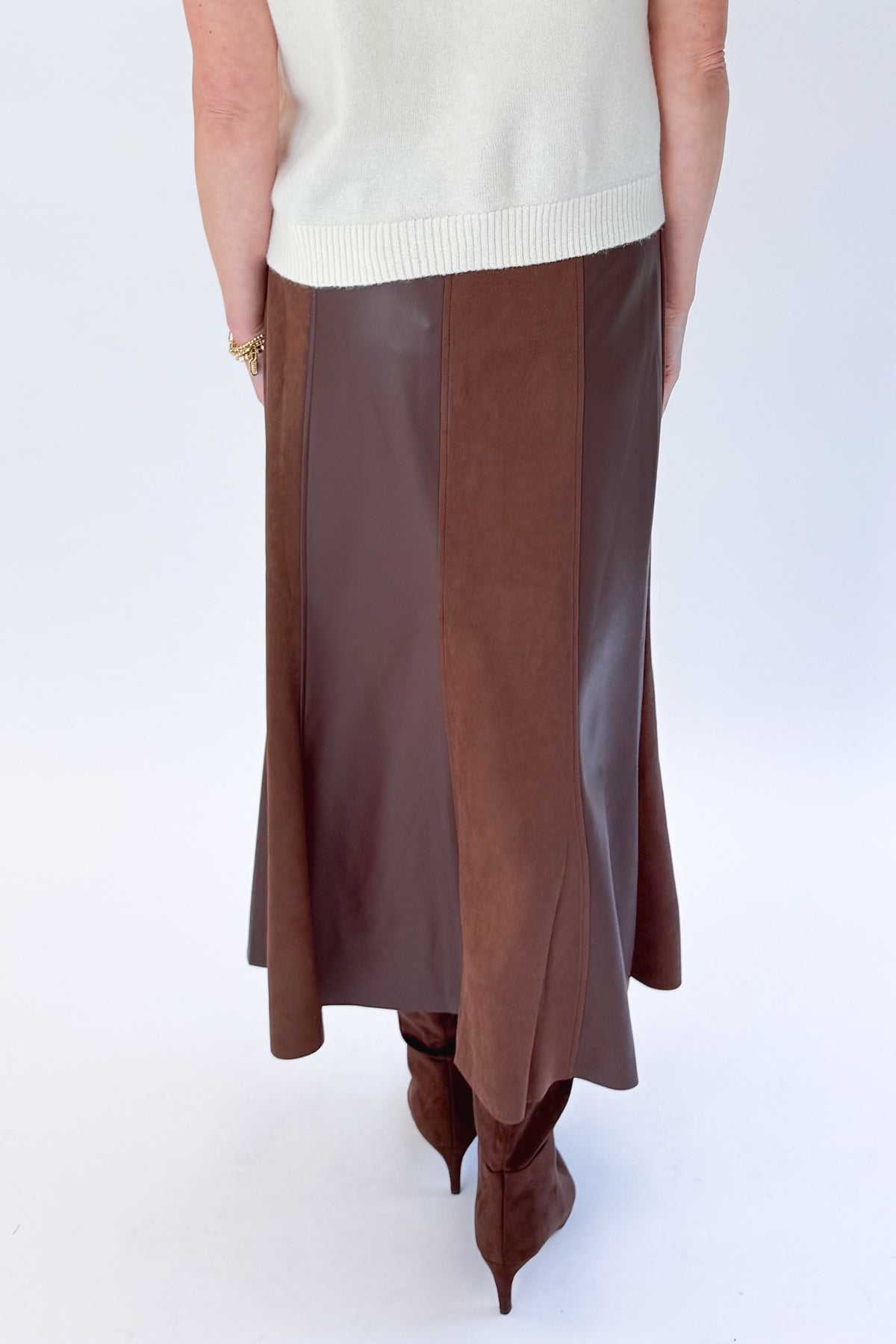 Back detail view of woman wearing Swagger Boutique’s Cream Sleeveless Button Up Sweater with Brown Suede &amp; Leather Midi Skirt by THML against white studio background.