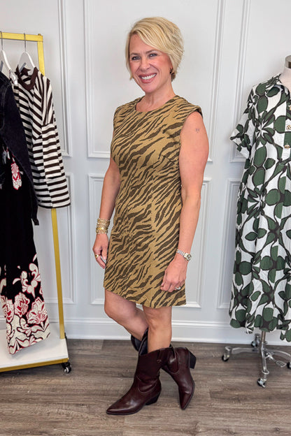 Side view of woman wearing Swagger Boutique’s Brown Tiger Print Mini Dress by Entro with boots with clothing hanging in the background.