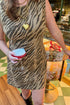 Front detail view of woman wearing Swagger Boutique’s Brown Tiger Print Mini Dress by Entro with boots at a bar.