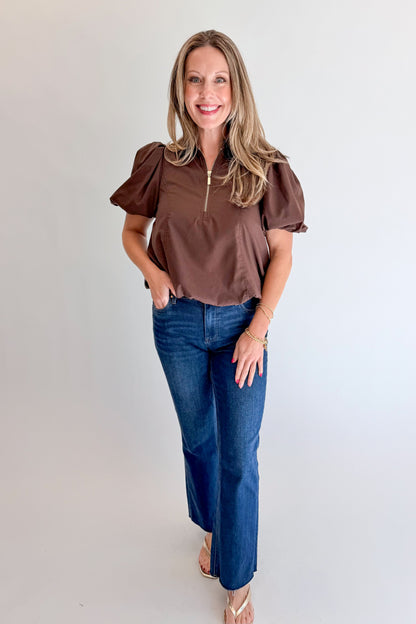 Front view of woman wearing Swagger Boutique’s Brown Zippered Bubble Hem Top by Entro with jeans against white studio background.