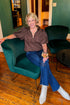 Front view of woman wearing Swagger Boutique’s Brown Zippered Bubble Hem Top by Entro with jeans sitting on a club chair. 
