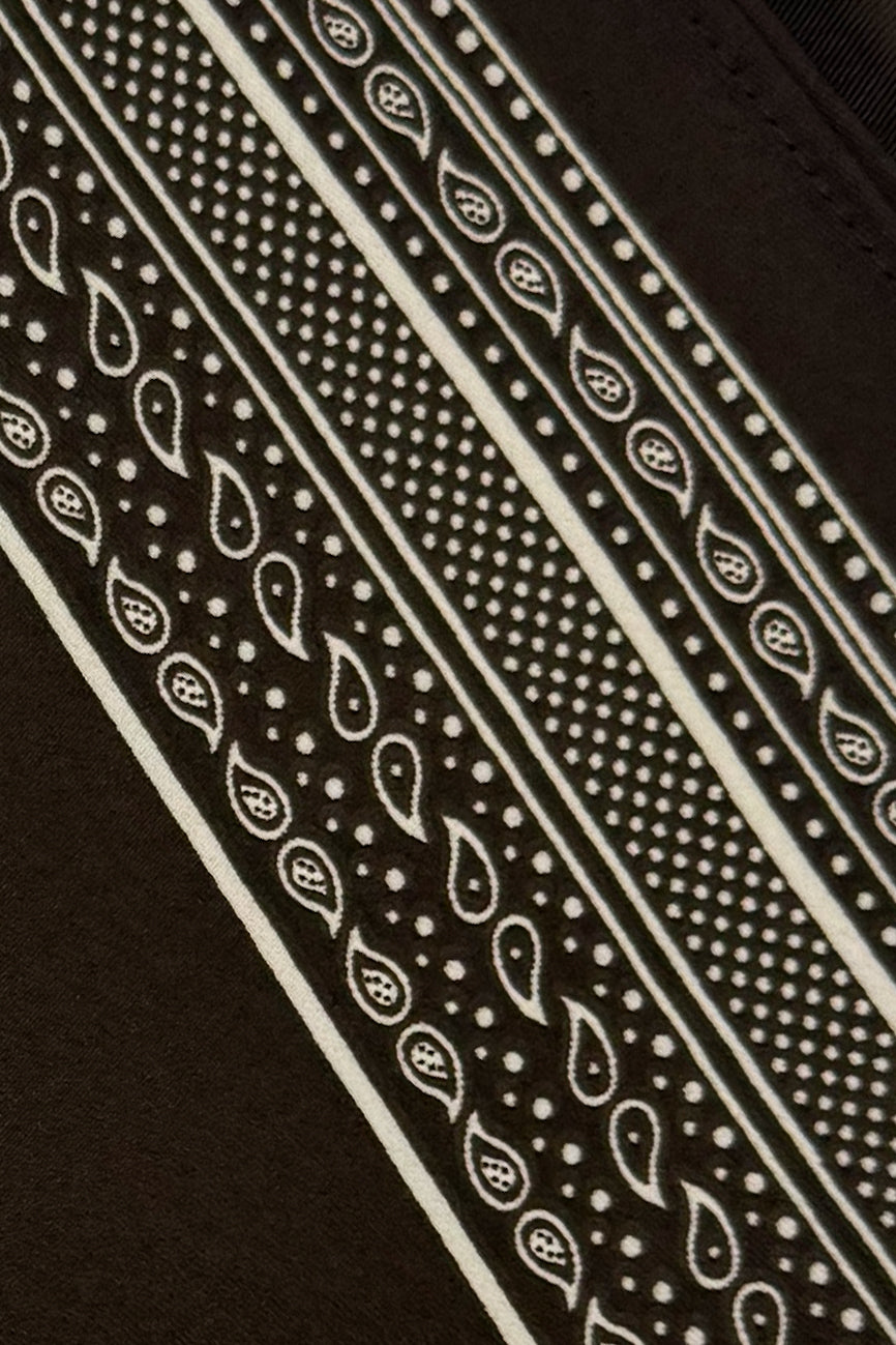 Close-up of a dark brown fabric with a cream paisley and dotted bandana-style pattern running diagonally across the frame.