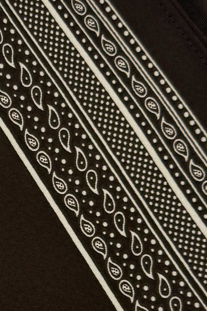 Close-up of a dark brown fabric with a cream paisley and dotted bandana-style pattern running diagonally across the frame.