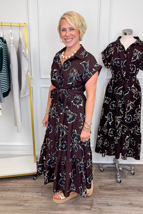 Side view of woman wearing Swagger Boutique’s Brown. &amp; Black Floral Print Midi Dress by Entro with clothing hanging in the background.