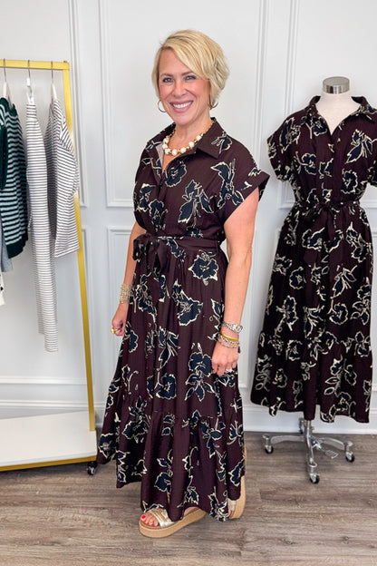 Side view of woman wearing Swagger Boutique’s Brown. &amp; Black Floral Print Midi Dress by Entro with clothing hanging in the background.