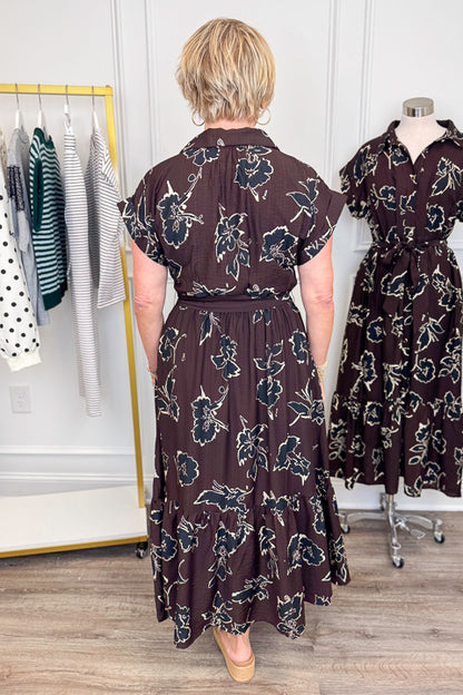 Back view of woman wearing Swagger Boutique’s Brown. &amp; Black Floral Print Midi Dress by Entro with clothing hanging in the background.