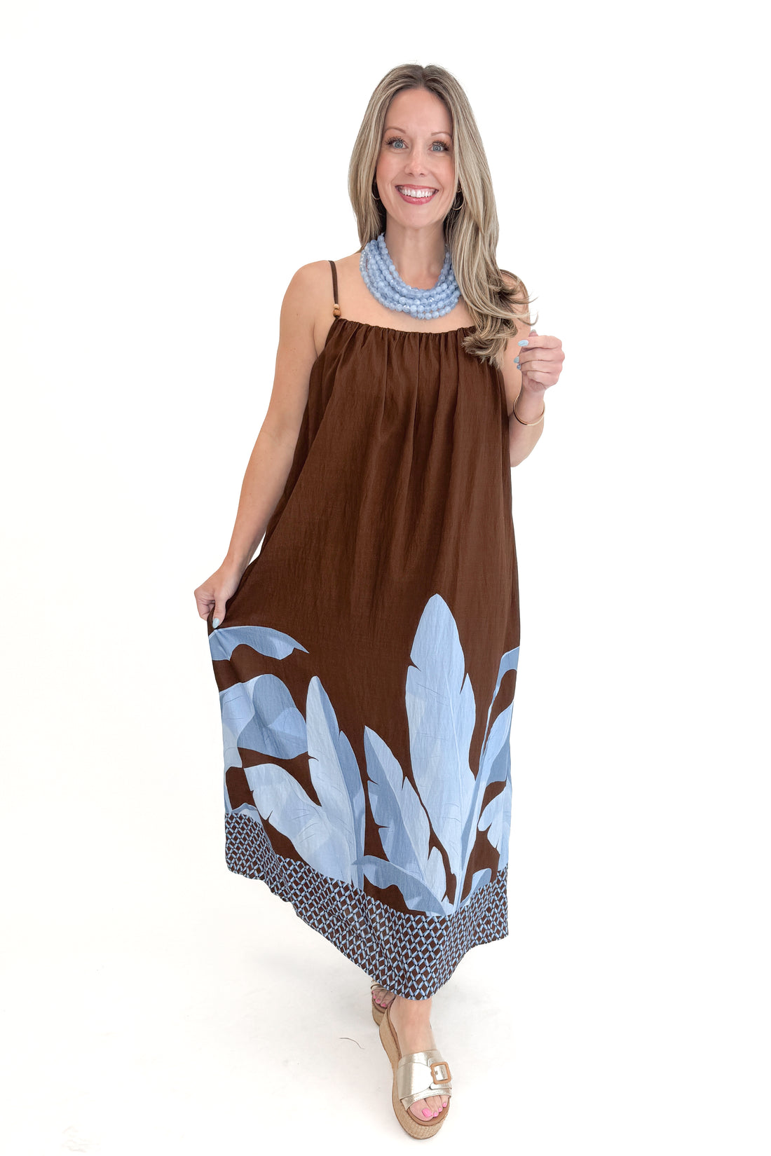 Front view of woman wearing Brown &amp; Blue Floral Maxi Dress with gold sandals against white studio background.