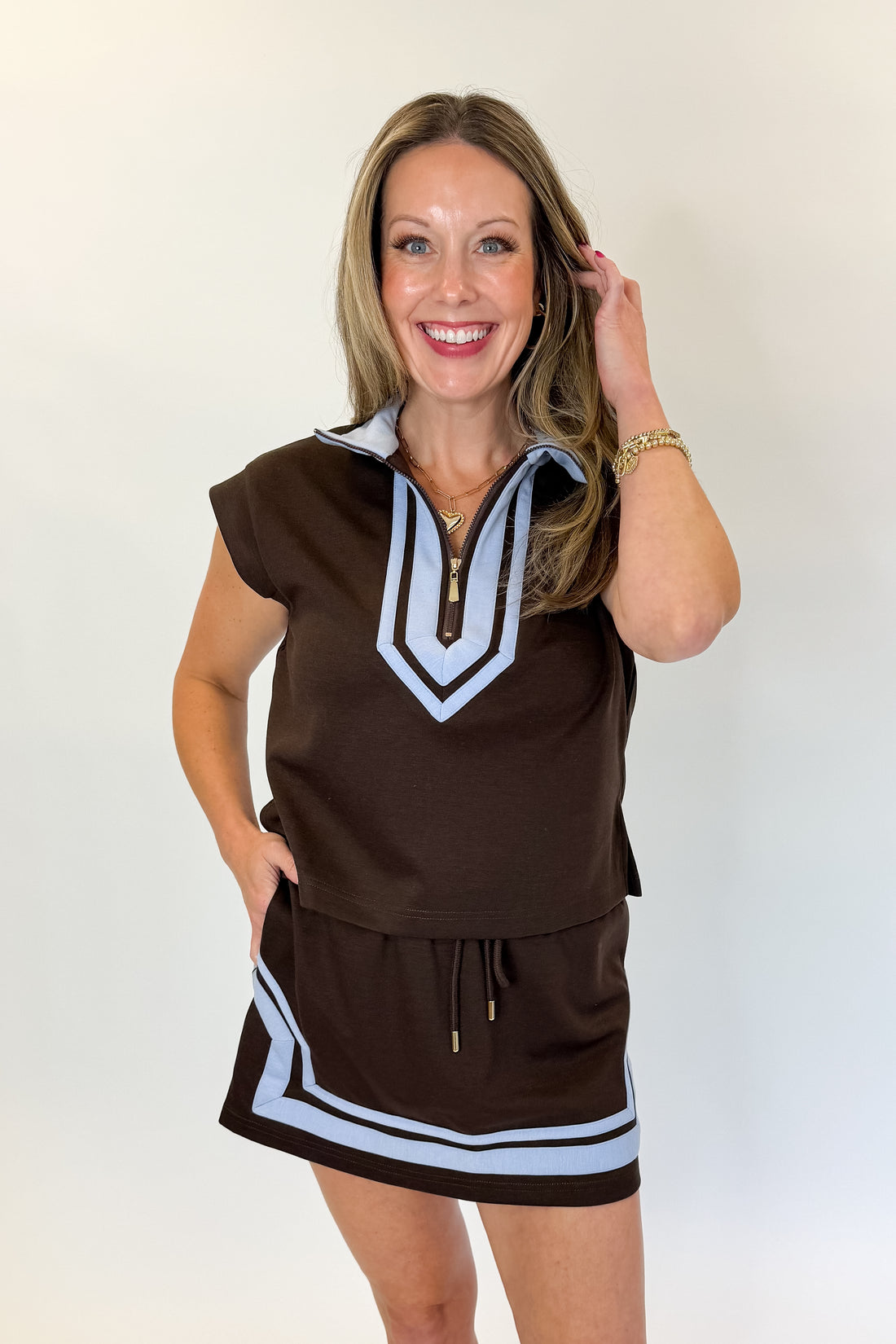 Front view of woman wearing Swagger Boutique’s Brown &amp; Blue Mini Skirt and Half Zip Top by Entro against white studio background.