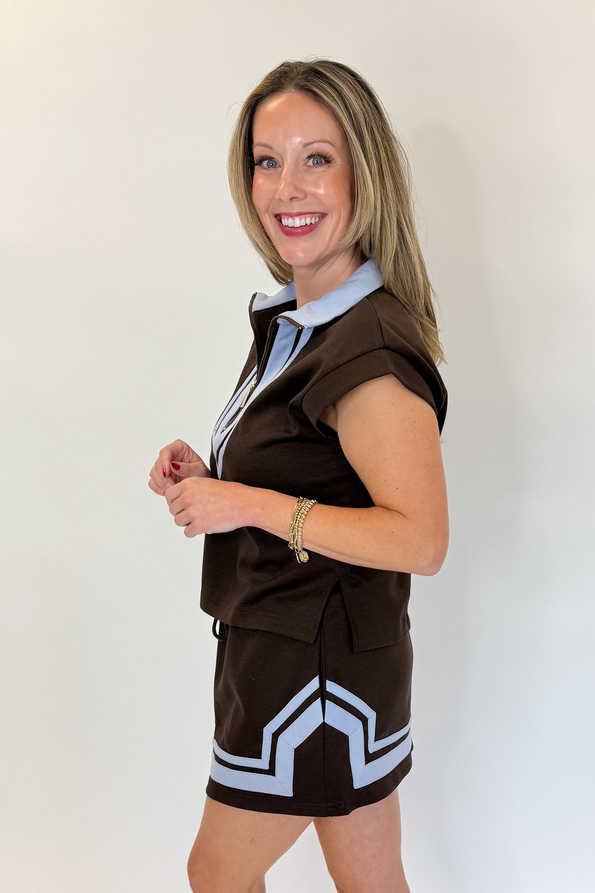 Side view of woman wearing Swagger Boutique’s Brown &amp; Blue Mini Skirt and Half Zip Top by Entro against white studio background.