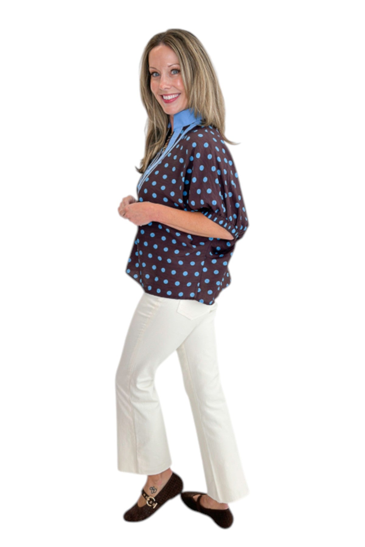 Side view of woman wearing Swagger Boutique’s Brown &amp; Blue Polka Dot Dolman Sleeve Top by Entro with jeans against white studio background.