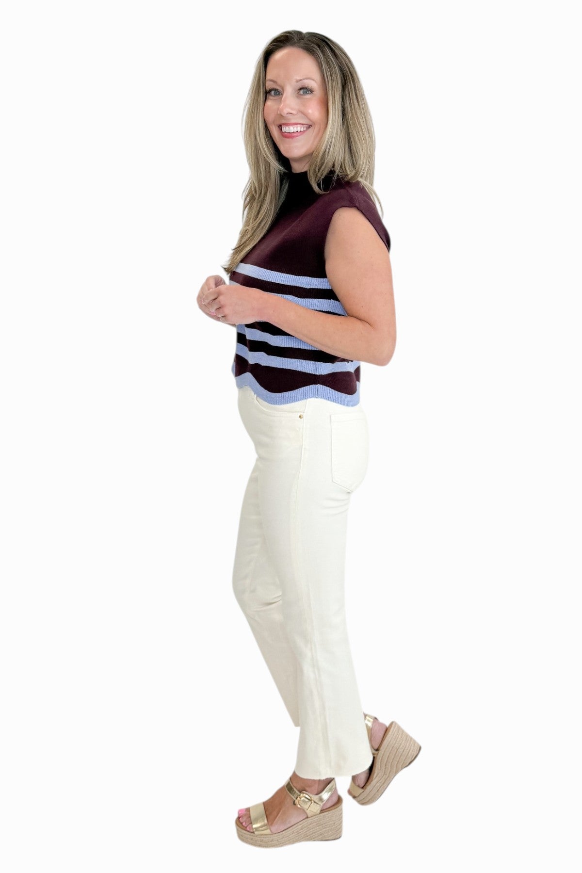Side view of woman wearing Swagger Boutique’s Brown &amp; Blue Scallop Hem Sleeveless Sweater by Entro with jeans against white studio background.