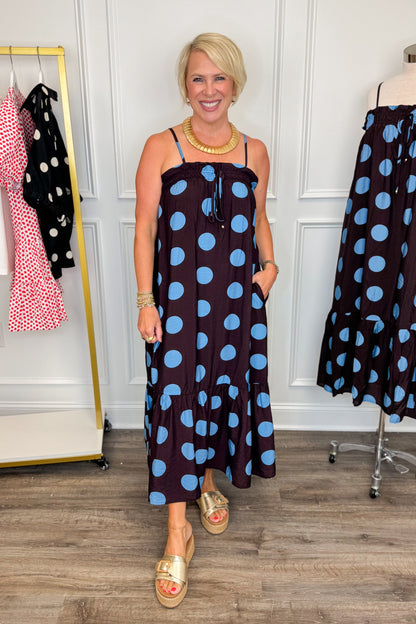 Front view of woman wearing Swagger Boutique’s Works Every Time Brown &amp; Blue Polka Dot Midi Dress by Entro with clothing hanging in the background.