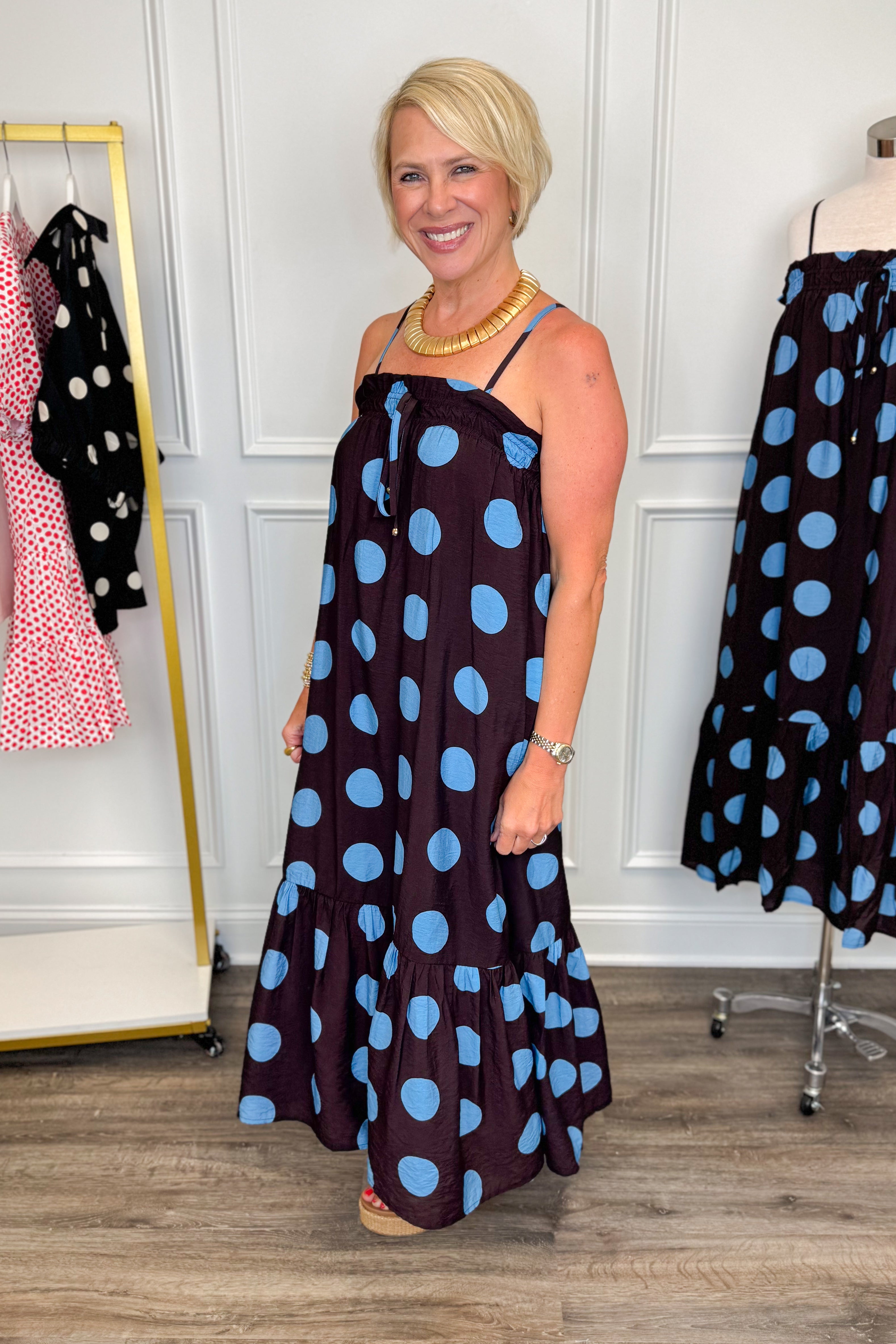 Side view of woman wearing Swagger Boutique’s Works Every Time Brown &amp; Blue Polka Dot Midi Dress by Entro with clothing hanging in the background.