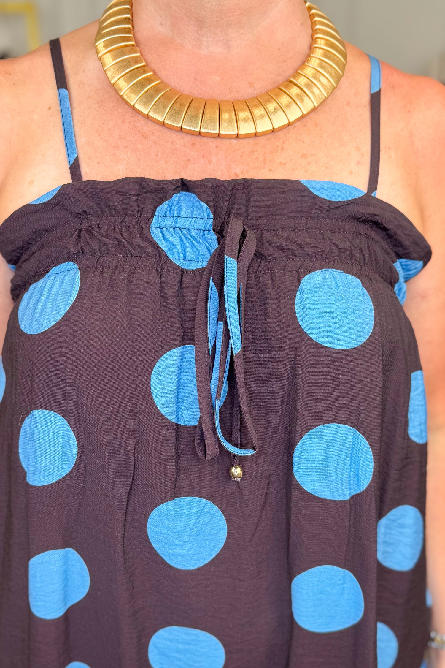 Front detail view of woman wearing Swagger Boutique’s Works Every Time Brown &amp; Blue Polka Dot Midi Dress by Entro with clothing hanging in the background.