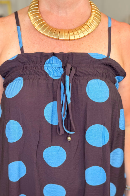 Front detail view of woman wearing Swagger Boutique’s Works Every Time Brown &amp; Blue Polka Dot Midi Dress by Entro with clothing hanging in the background.
