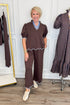 Front view of woman wearing Swagger Boutique’s Brown & Blue Scalloped Top by Entro with matching pants with clothing hanging in the background.