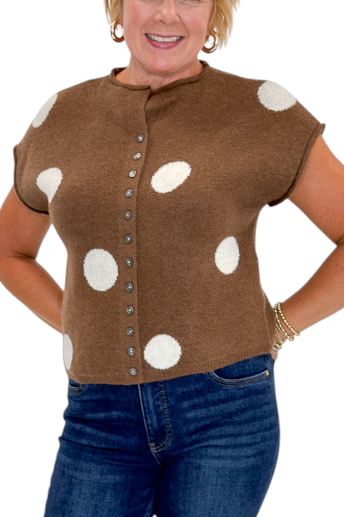 Front detail view of woman wearing Swagger Boutique’s Brown &amp; Cream Polka Dot Sleeveless Button Up Sweater by Entro with jeans against white studio background.