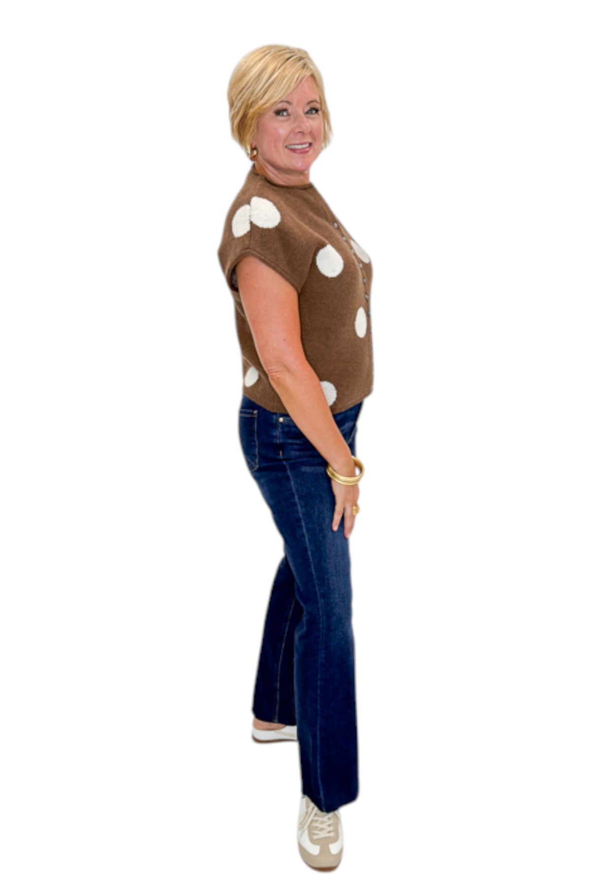 Side view of woman wearing Swagger Boutique’s Brown &amp; Cream Polka Dot Sleeveless Button Up Sweater by Entro with jeans against white studio background.