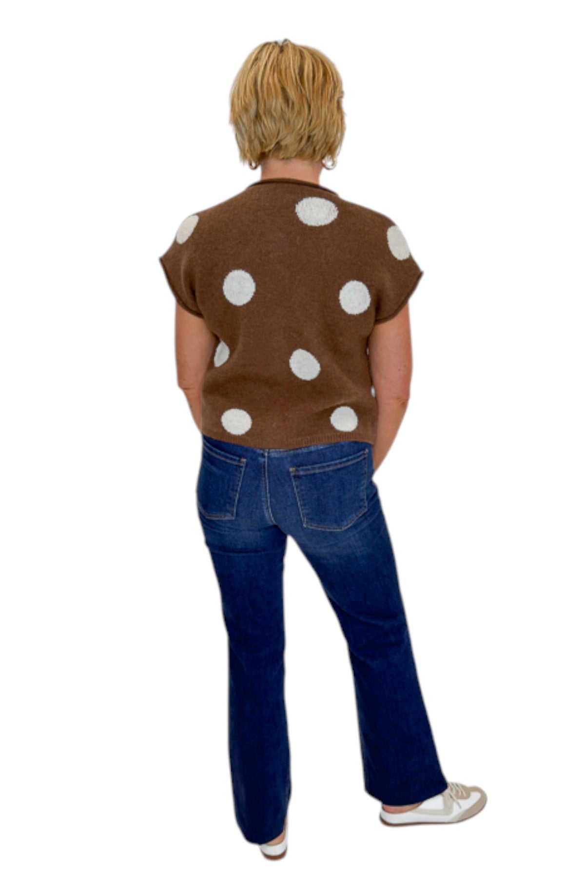 Back view of woman wearing Swagger Boutique’s Brown &amp; Cream Polka Dot Sleeveless Button Up Sweater by Entro with jeans against white studio background.