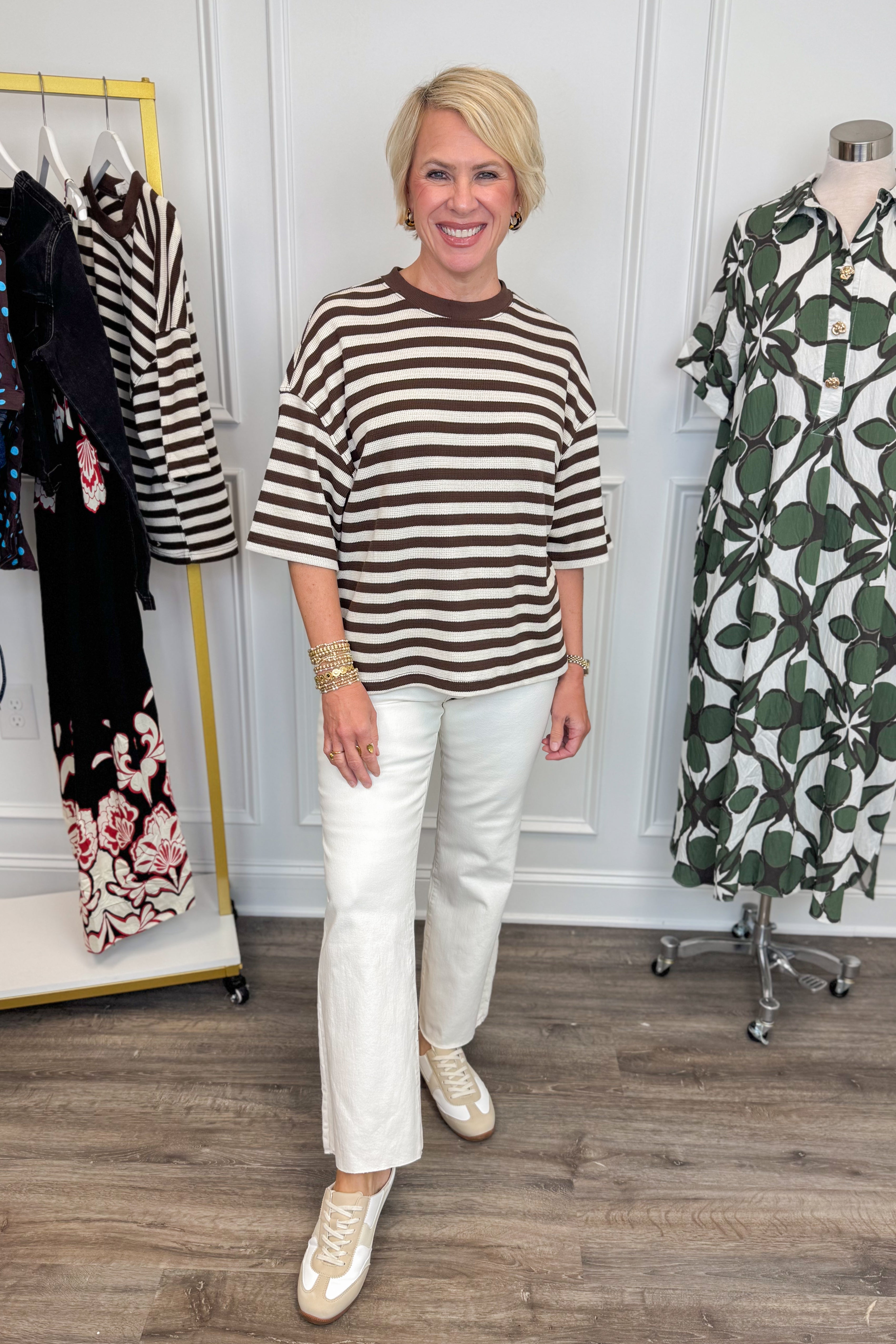 Front view of woman wearing Swagger Boutique’s Brown &amp; Cream Striped Textured Tee by Entro with jeans with clothing hanging in the background. 
