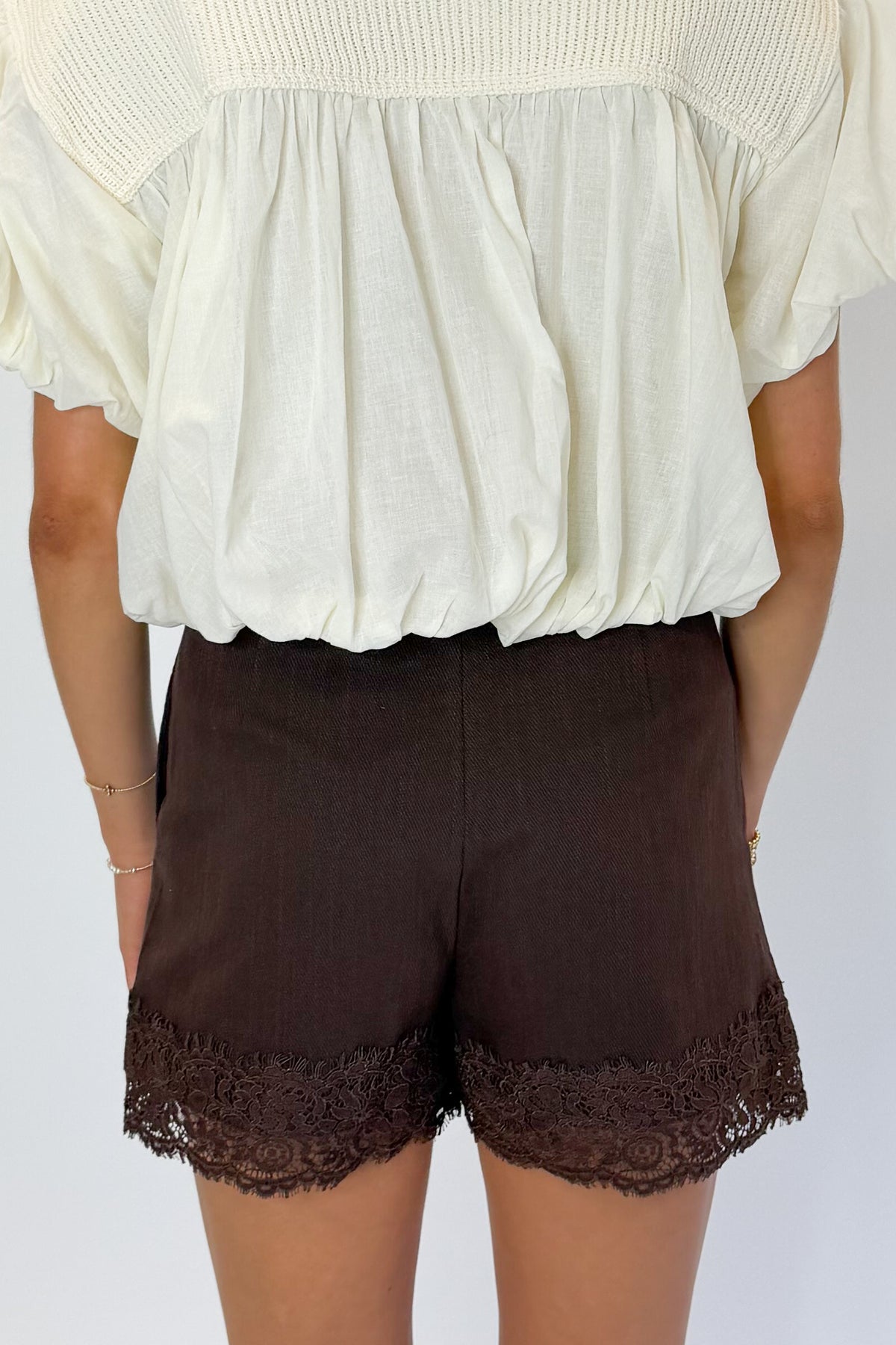 Back view of woman wearing Swagger Boutique’s Brown Lace Lined Denim Skort with top against white studio background.