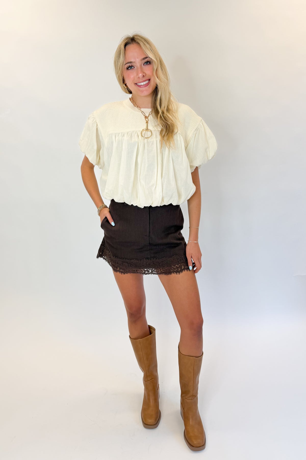 Front view of woman wearing Swagger Boutique’s Brown Lace Lined Denim Skort with Cream Mixed Material Bubble Hem Top against white studio background.