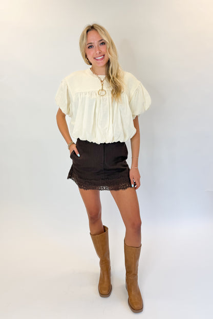 Front view of woman wearing Swagger Boutique’s Brown Lace Lined Denim Skort with Cream Mixed Material Bubble Hem Top against white studio background.