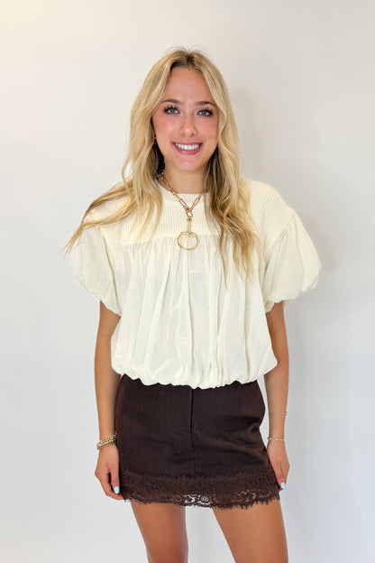 Front view of woman wearing Swagger Boutique’s Brown Lace Lined Denim Skort with Cream Mixed Material Bubble Hem Top against white studio background.