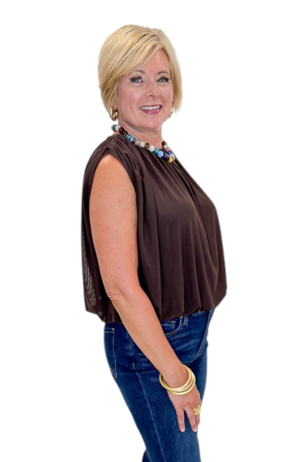 Side view of woman wearing Swagger Boutique’s Brown Mesh Bubble Hem Top with jeans against white studio background.