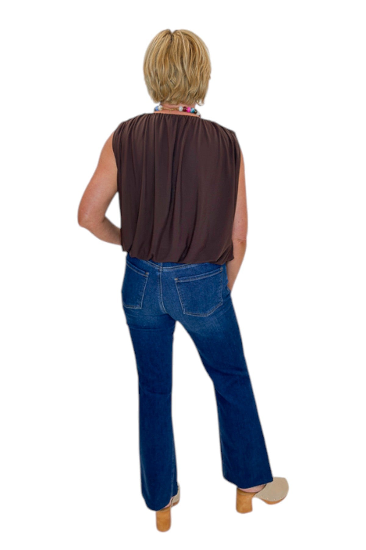 Back view of woman wearing Swagger Boutique’s Brown Mesh Bubble Hem Top with jeans against white studio background.