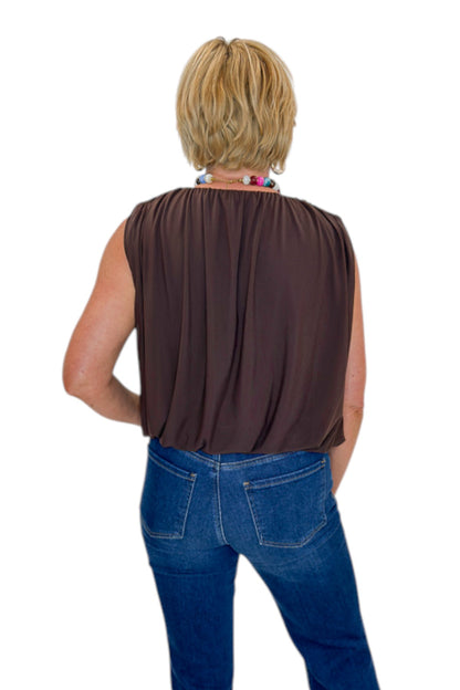 Back view of woman wearing Swagger Boutique’s Brown Mesh Bubble Hem Top with jeans against white studio background.