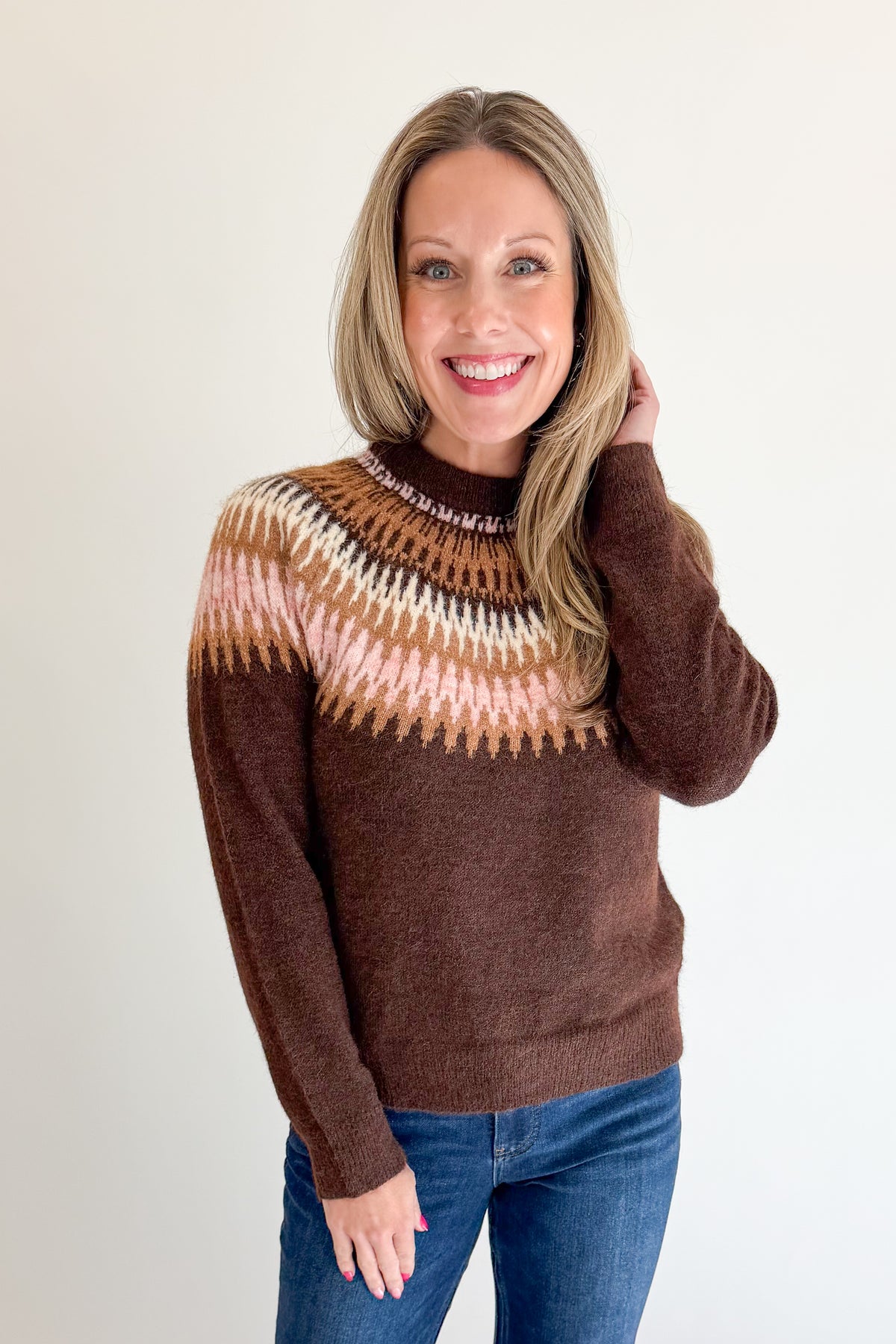 Front view of woman wearing Swagger Boutique’s Brown &amp; Pink Fair Isle Sweater with jeans against white studio background.