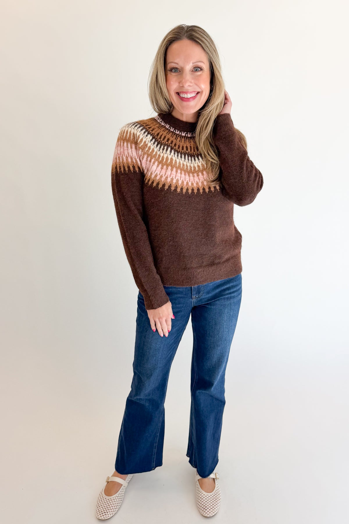 Front view of woman wearing Swagger Boutique’s Brown &amp; Pink Fair Isle Sweater with jeans against white studio background.