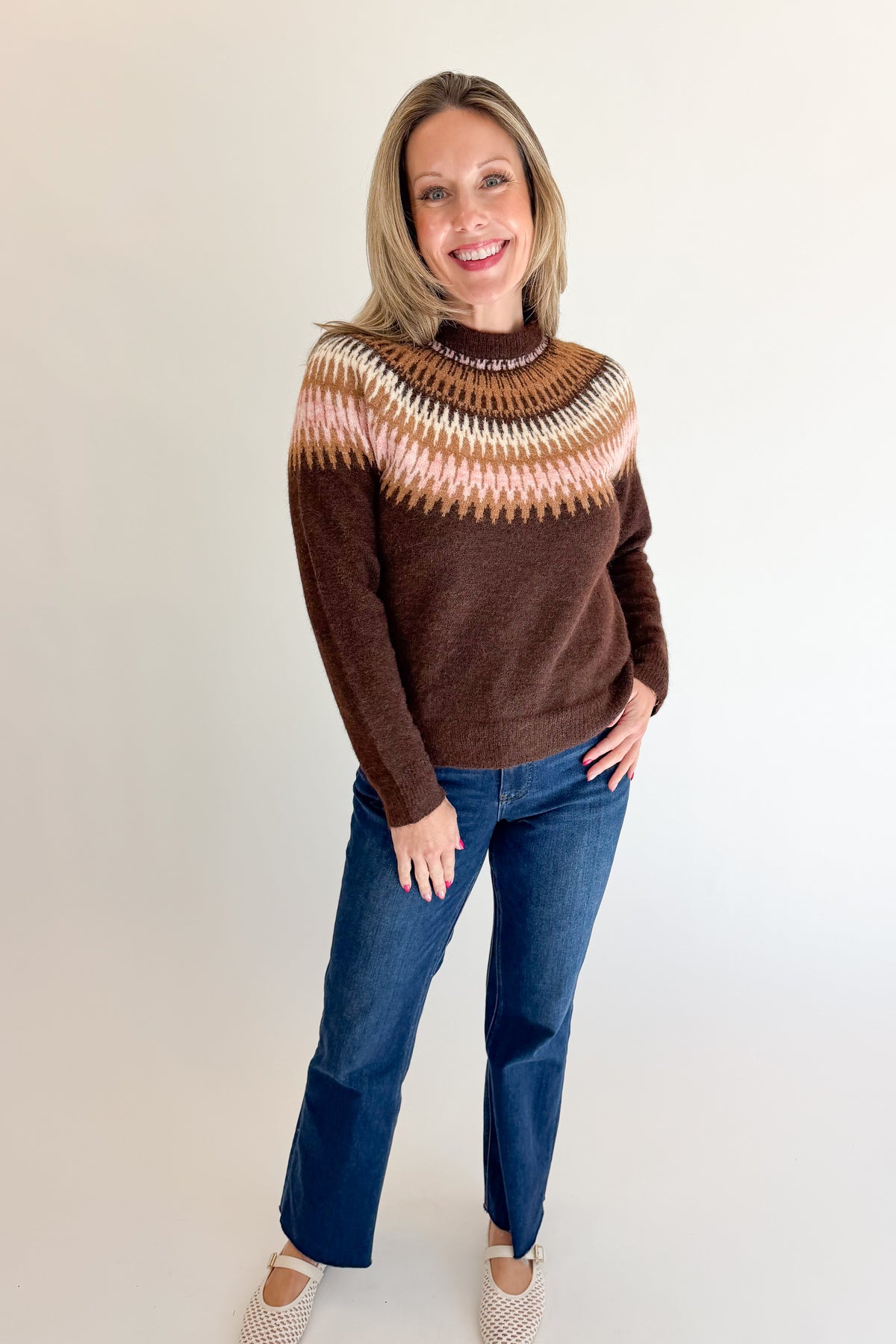 Front view of woman wearing Swagger Boutique’s Brown &amp; Pink Fair Isle Sweater with jeans against white studio background.