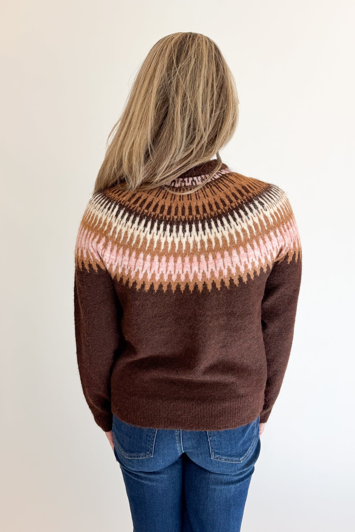 Back view of woman wearing Swagger Boutique’s Brown &amp; Pink Fair Isle Sweater with jeans against white studio background.
