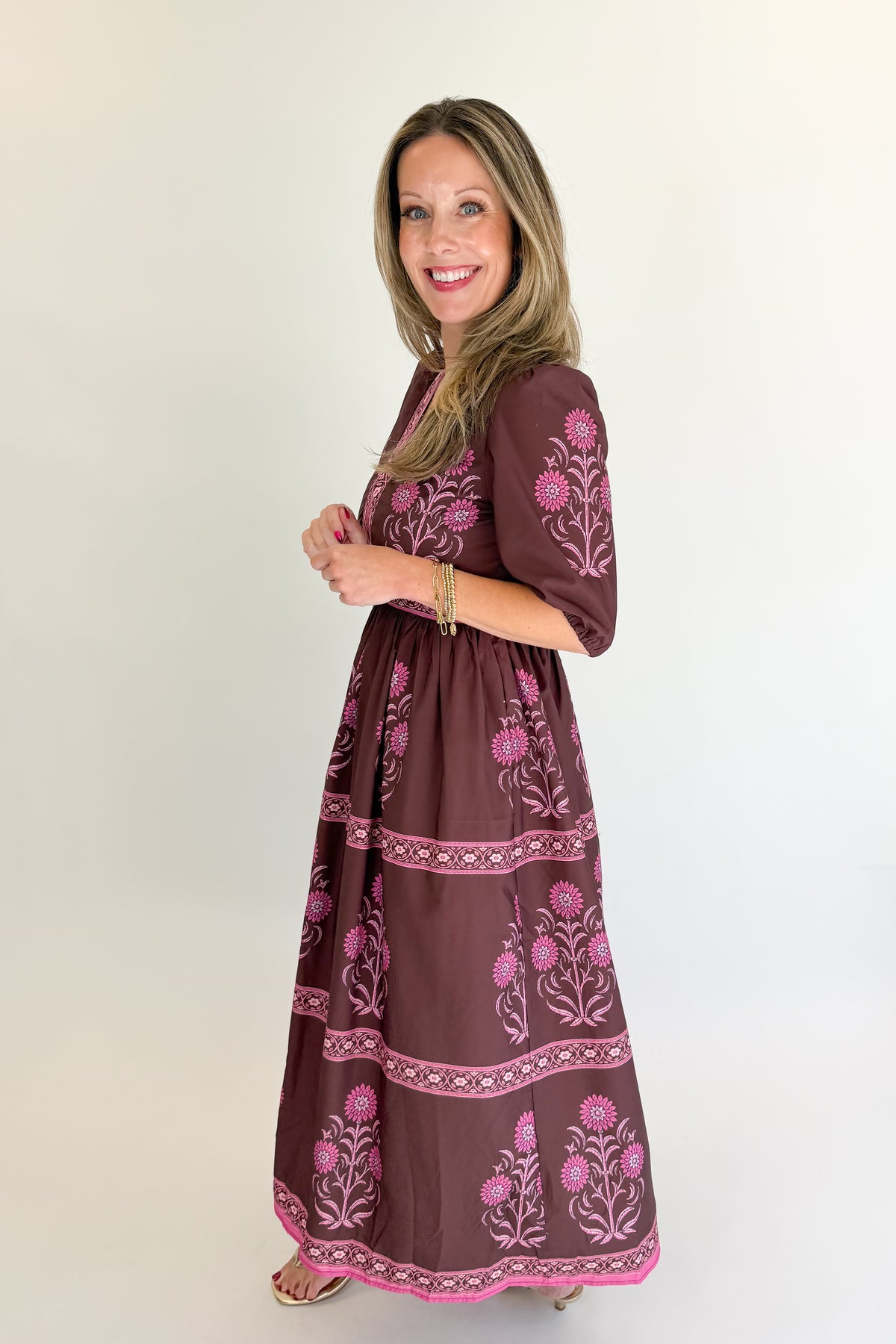 Side view of woman wearing Swagger Boutique’s Brown &amp; Pink Printed Midi Dress with heels against white studio background.