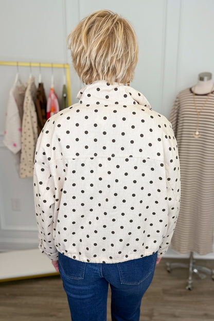 Back view of woman wearing Swagger Boutique’s Brown Polka Dot Denim Jacket with jeans with clothing hanging in the background.