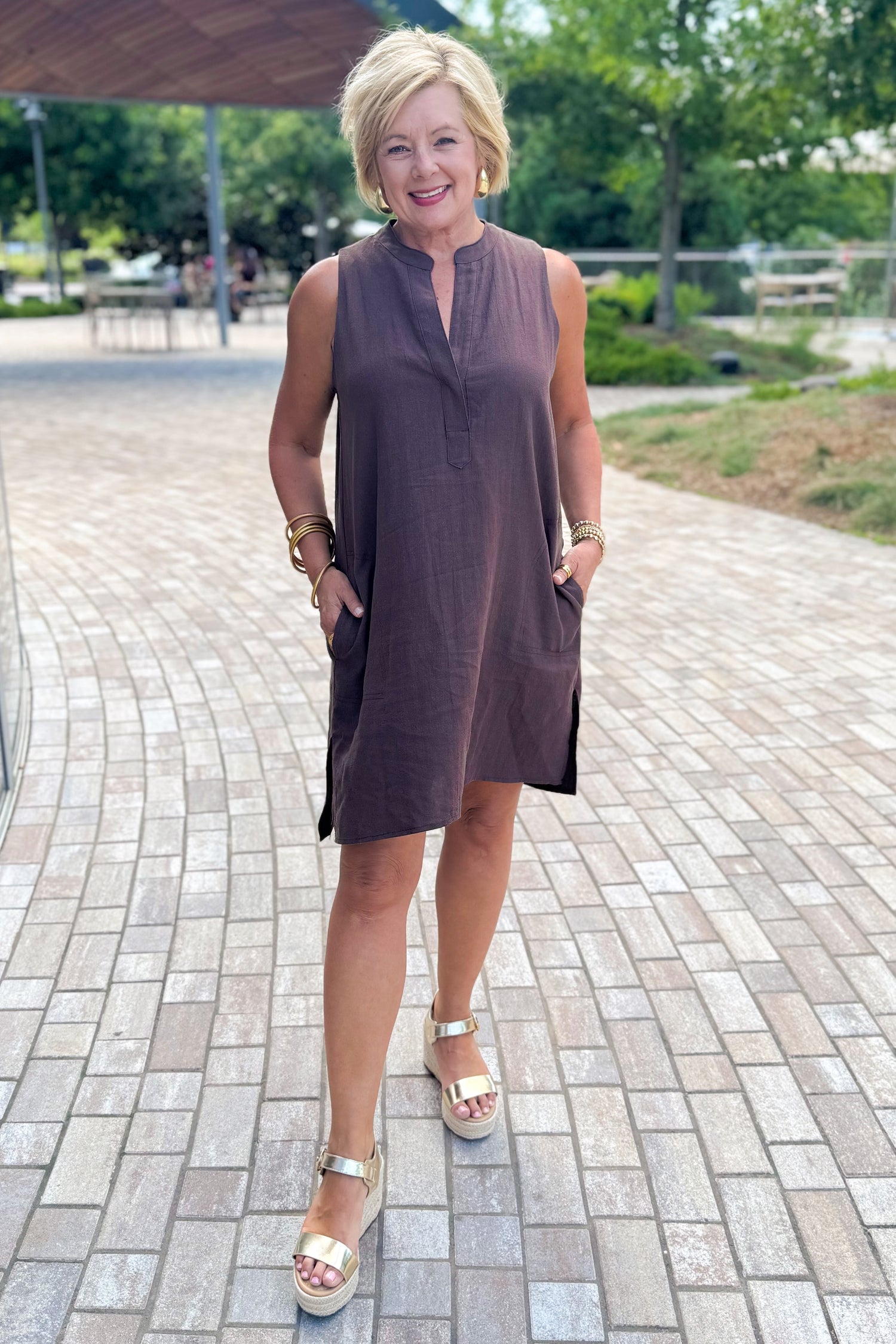 Woman wearing a brown dress standing outside at a park.