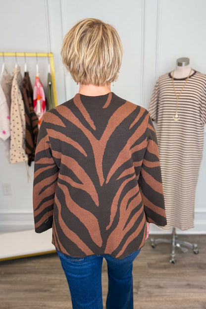 Back view of woman wearing Swagger Boutique’s Brown Zebra Mock Neck Sweater with jeans with clothing hanging in the background.
