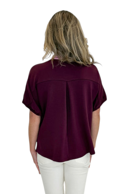 Back view of woman wearing Swagger Boutique’s Burgundy &amp; Pink Contrast Dolman Sleeve Top by Entro with jeans against white studio background.
