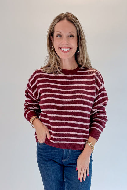 Front view of woman wearing Swagger Boutique’s Burgundy &amp; Pink Striped Sweater with jeans against white studio background.