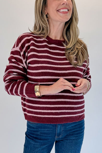 Front detail view of woman wearing Swagger Boutique’s Burgundy &amp; Pink Striped Sweater with jeans against white studio background.