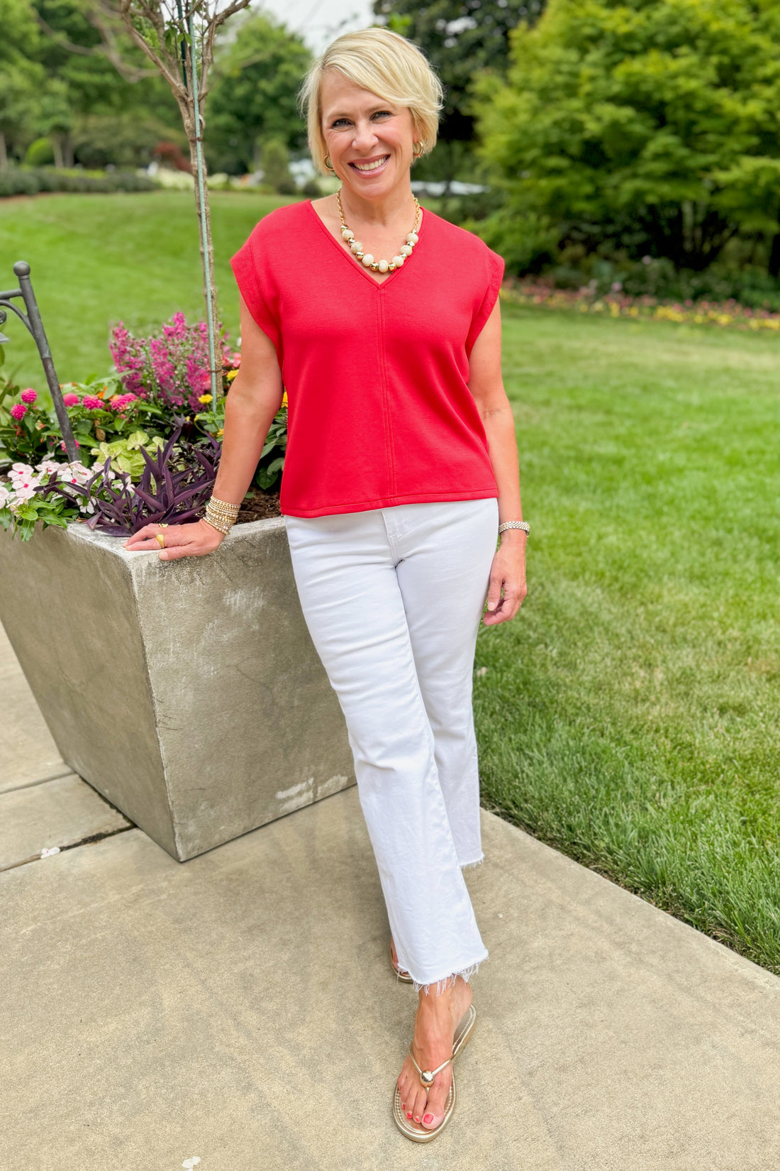 Front view of woman wearing Swagger Boutique’s Red V-Neck Tank by Entro with jeans standing outside at a park.