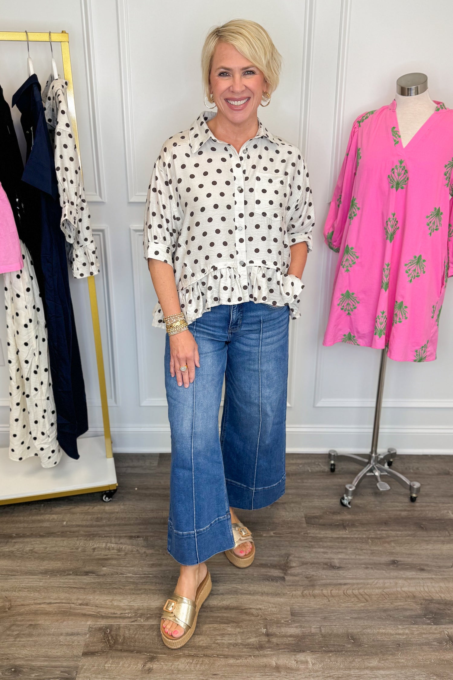 Front view of woman wearing Swagger Boutique’s Cream &amp; Brown Polka Dot Peplum Top by Entro with jeans with clothes around her.