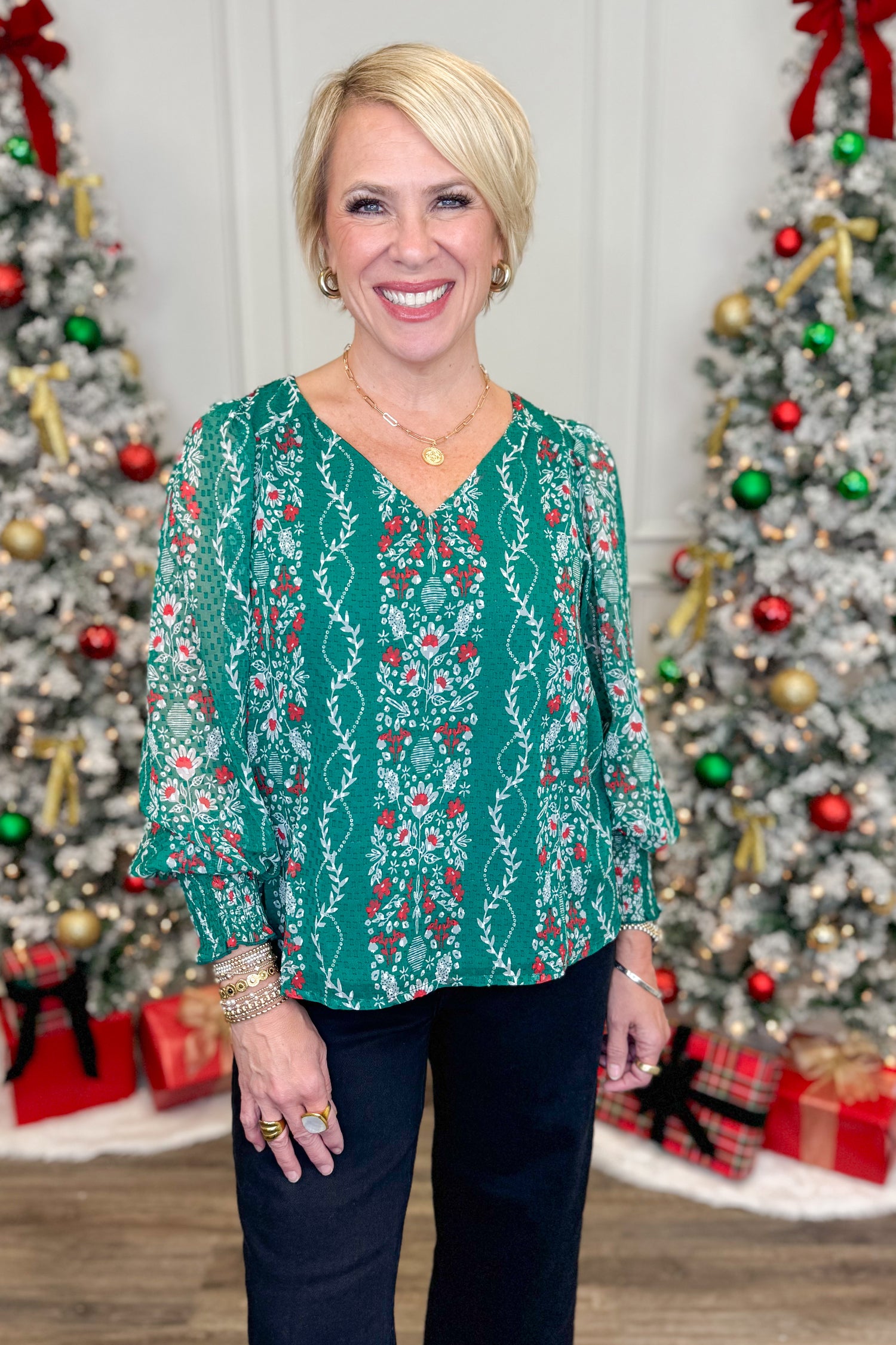 Woman wearing a green patterned blouse in front of Christmas trees with decorations.
